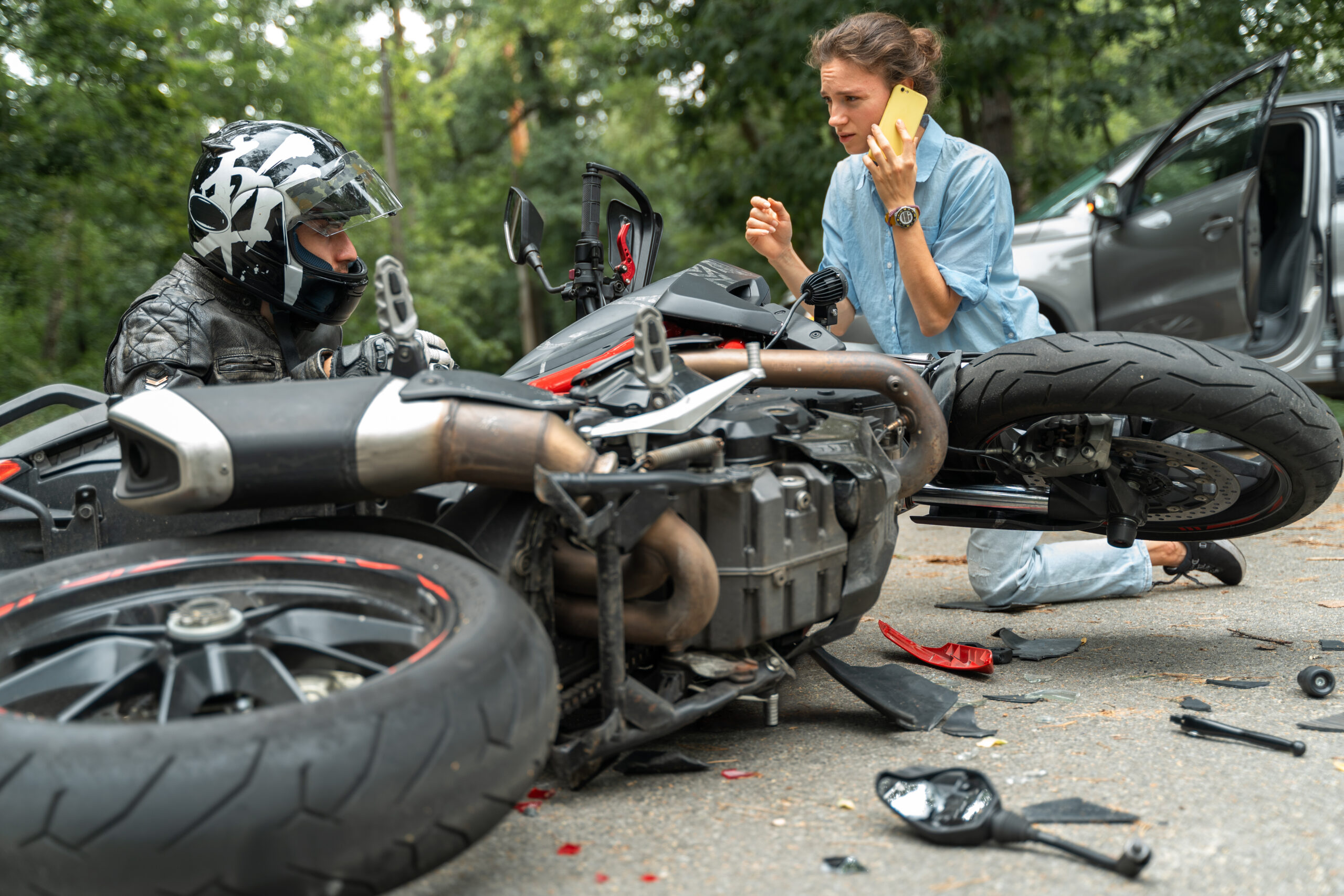 Collision between motorcycle and car on the road. Girl driver hit motorcyclist and uses her phone to call for help. Broken and wrecked motorcycle on road